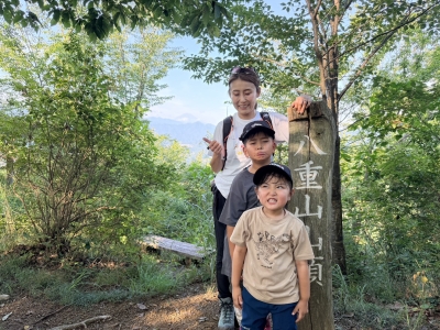 八重山山頂の標識前で上野原の山並みを背にする親子